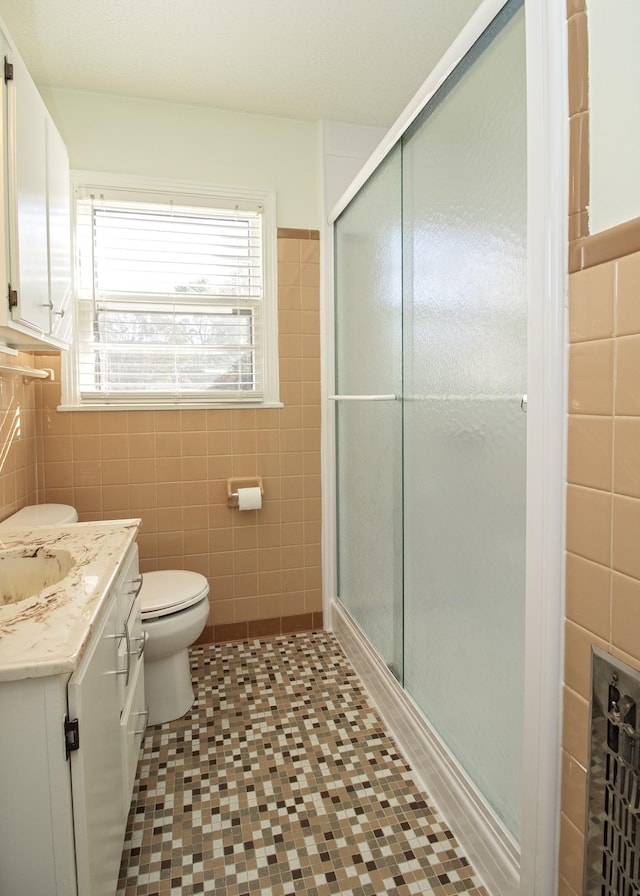 bathroom with toilet, vanity, a shower stall, and tile walls