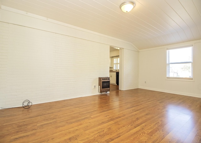 unfurnished living room with a wealth of natural light, brick wall, heating unit, and wood finished floors