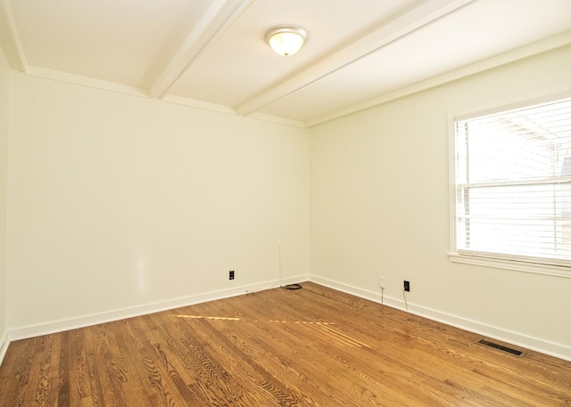 unfurnished room with baseboards, visible vents, beamed ceiling, and wood finished floors