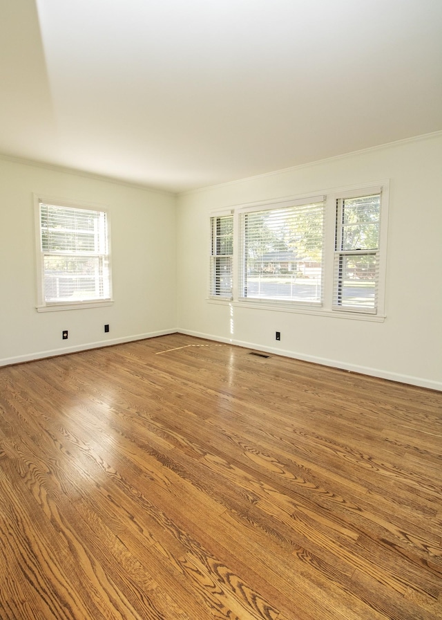 unfurnished room with baseboards, plenty of natural light, visible vents, and wood finished floors