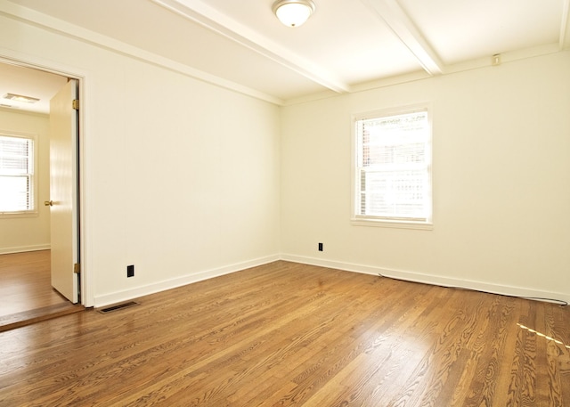 spare room with beamed ceiling, wood finished floors, visible vents, and baseboards