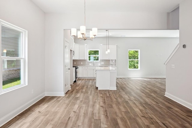 kitchen with a sink, white cabinets, light countertops, tasteful backsplash, and decorative light fixtures