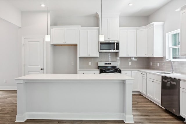 kitchen with a center island, stainless steel appliances, light countertops, pendant lighting, and a sink