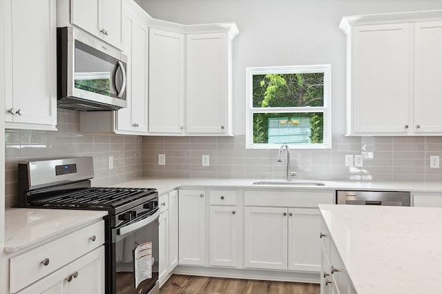 kitchen with stainless steel appliances, white cabinetry, a sink, and light stone counters