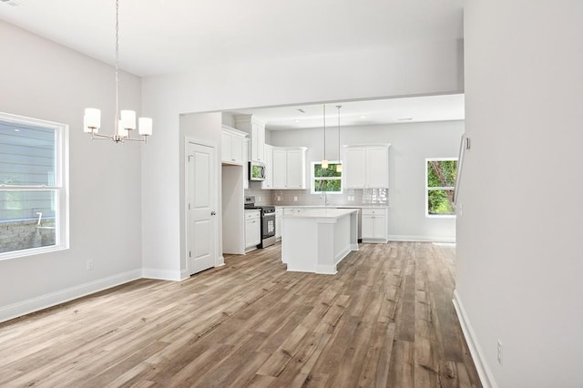 kitchen with a center island, decorative light fixtures, stainless steel appliances, light countertops, and white cabinets