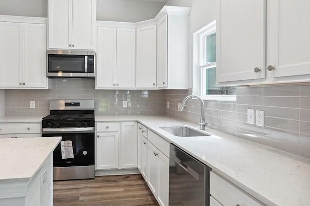 kitchen featuring light stone counters, dark wood finished floors, appliances with stainless steel finishes, white cabinets, and a sink