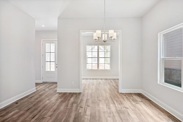 unfurnished dining area with light wood-style floors, baseboards, and an inviting chandelier