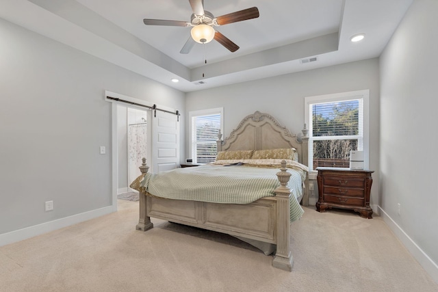 bedroom featuring a barn door, light colored carpet, visible vents, baseboards, and a raised ceiling