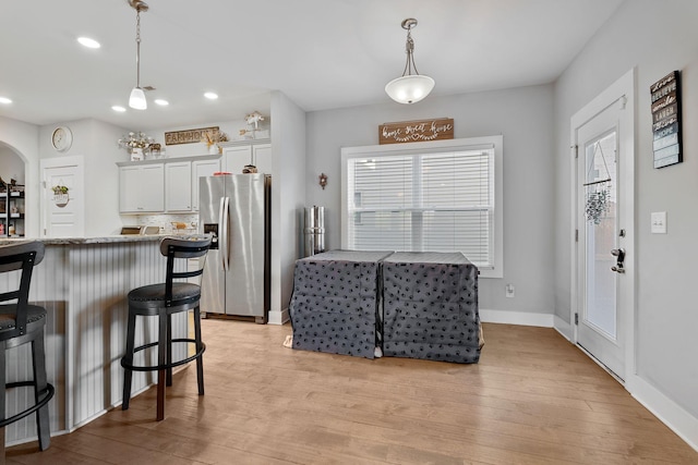 kitchen featuring white cabinets, stainless steel fridge with ice dispenser, a breakfast bar, light stone countertops, and pendant lighting