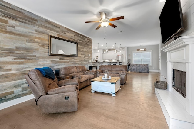 living room with a fireplace with raised hearth, an accent wall, visible vents, a ceiling fan, and light wood finished floors