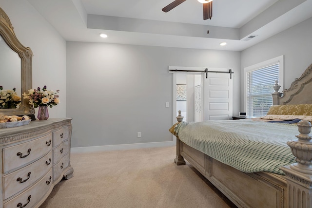 bedroom featuring light carpet, a tray ceiling, a barn door, and baseboards