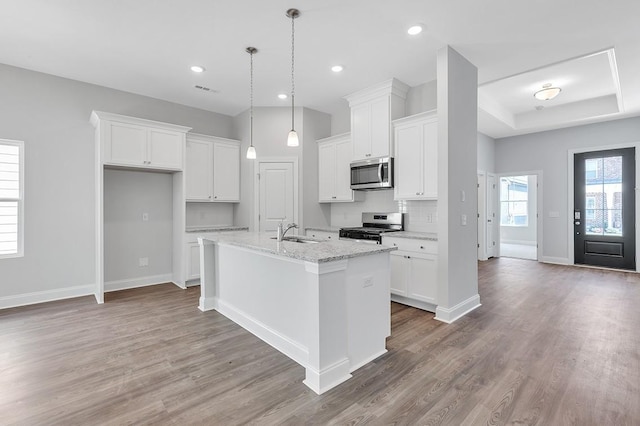 kitchen with an island with sink, appliances with stainless steel finishes, light stone countertops, white cabinetry, and a sink