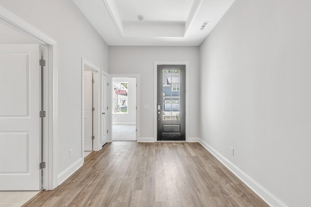 entrance foyer with light wood-type flooring, baseboards, visible vents, and a tray ceiling