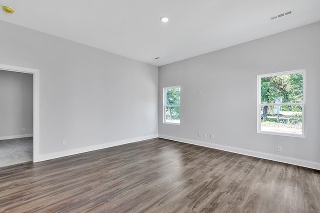 empty room featuring dark wood-type flooring, visible vents, and baseboards