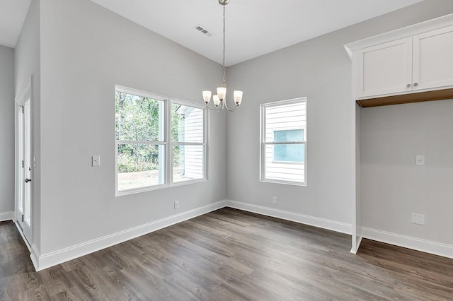 unfurnished dining area featuring dark wood-style flooring, visible vents, a notable chandelier, and baseboards