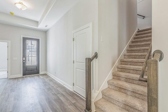 foyer with wood finished floors, visible vents, baseboards, stairway, and a tray ceiling