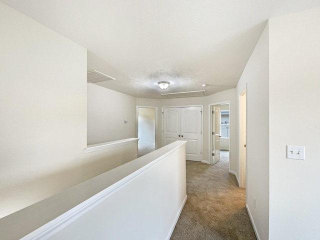 hall featuring carpet floors, visible vents, a textured ceiling, an upstairs landing, and baseboards