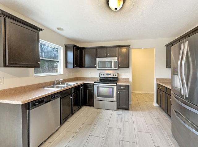 kitchen featuring baseboards, appliances with stainless steel finishes, light countertops, dark brown cabinets, and a sink