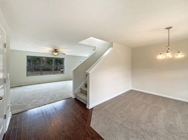 interior space featuring ceiling fan with notable chandelier, dark wood-type flooring, baseboards, stairway, and dark carpet