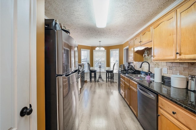 kitchen featuring pendant lighting, decorative backsplash, appliances with stainless steel finishes, light wood-style floors, and a sink