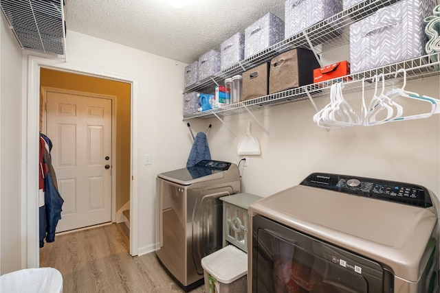 washroom featuring laundry area, light wood finished floors, visible vents, a textured ceiling, and separate washer and dryer