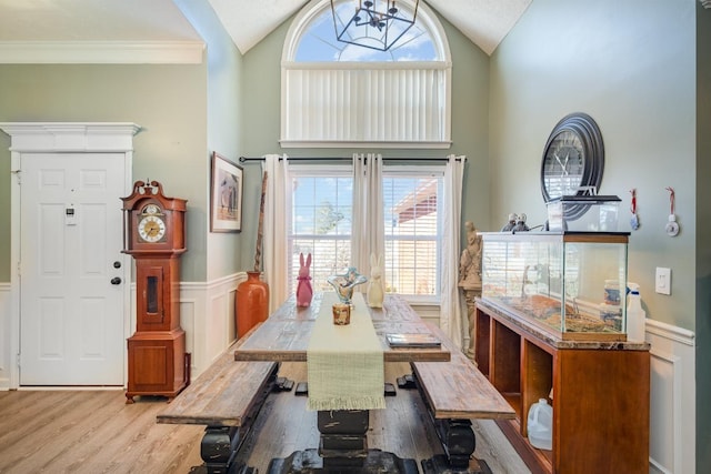 dining room featuring a chandelier, high vaulted ceiling, a decorative wall, wainscoting, and light wood finished floors