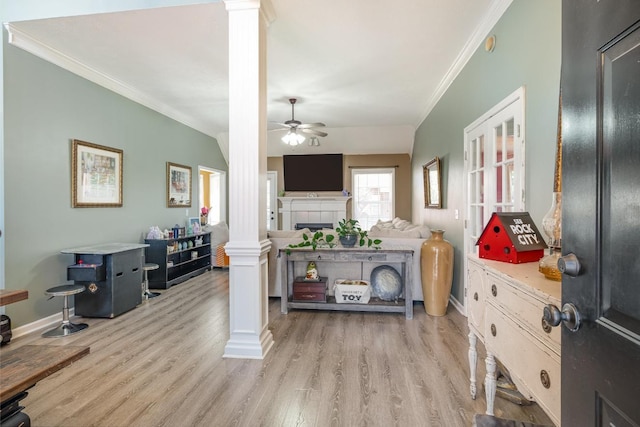 foyer entrance with crown molding, decorative columns, light wood-style flooring, a ceiling fan, and a tile fireplace