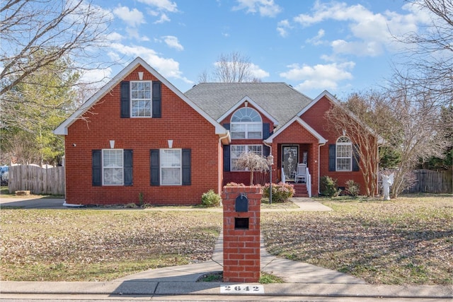 traditional-style home featuring brick siding, fence, and roof with shingles