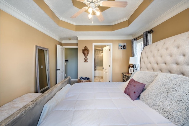 bedroom with a ceiling fan, a tray ceiling, crown molding, and ensuite bath