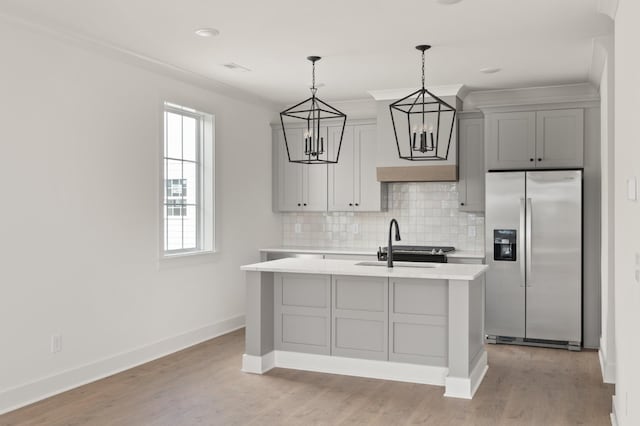 kitchen featuring a kitchen island with sink, light countertops, gray cabinets, stainless steel fridge with ice dispenser, and decorative light fixtures