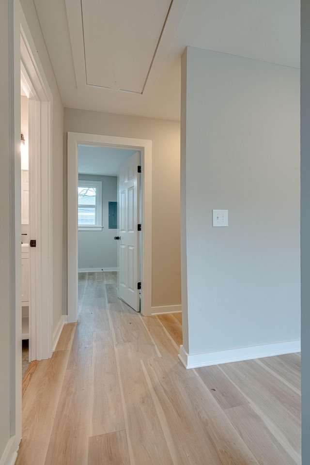 corridor featuring attic access, light wood-type flooring, and baseboards