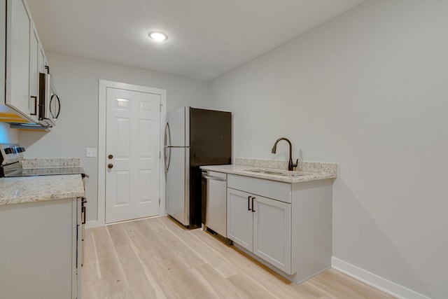 kitchen featuring stainless steel appliances, light wood finished floors, a sink, and light stone countertops