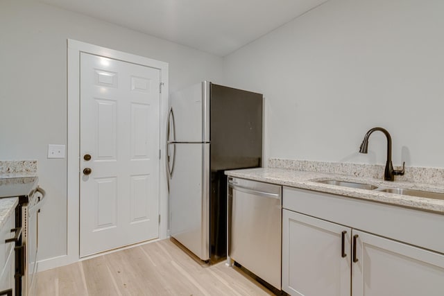 kitchen featuring a sink, white cabinets, light wood-style floors, appliances with stainless steel finishes, and light stone countertops