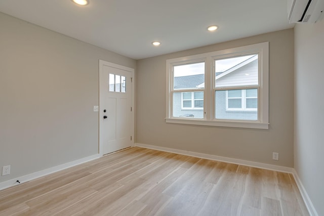 unfurnished room featuring light wood-type flooring, an AC wall unit, baseboards, and recessed lighting