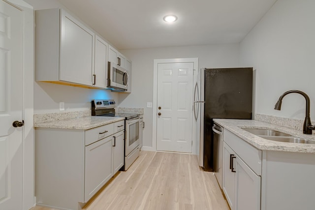 kitchen with appliances with stainless steel finishes, white cabinetry, a sink, light stone countertops, and light wood-type flooring