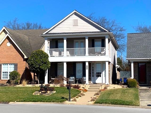 view of front of home featuring a balcony, brick siding, a porch, and a front yard