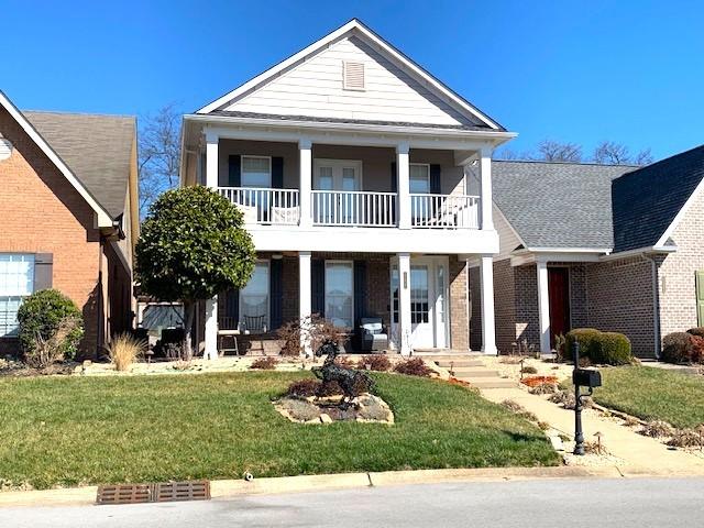 view of front of home featuring brick siding, a balcony, a porch, and a front yard