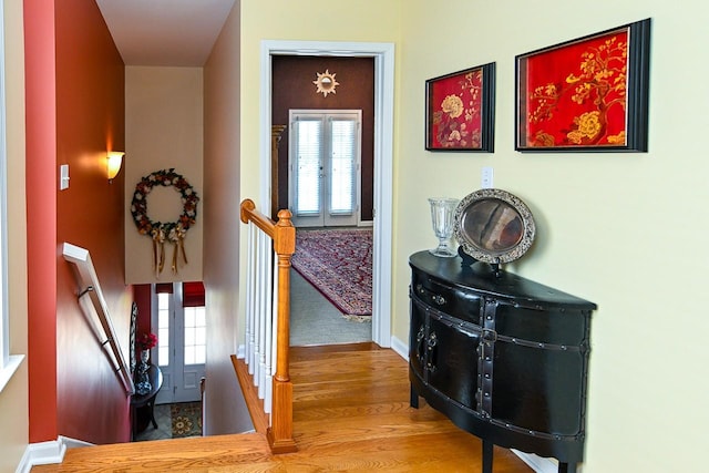 corridor with french doors, wood finished floors, an upstairs landing, and baseboards