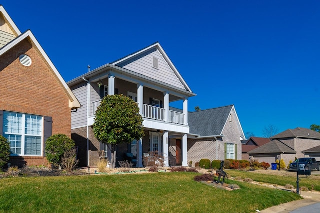 greek revival inspired property with a balcony, brick siding, a porch, and a front yard