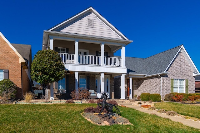 greek revival house with a front lawn, a porch, a shingled roof, a balcony, and brick siding