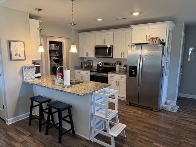 kitchen featuring stainless steel appliances, white cabinets, decorative light fixtures, and a sink