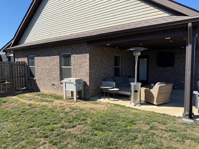 rear view of house with a yard, brick siding, a patio area, and fence