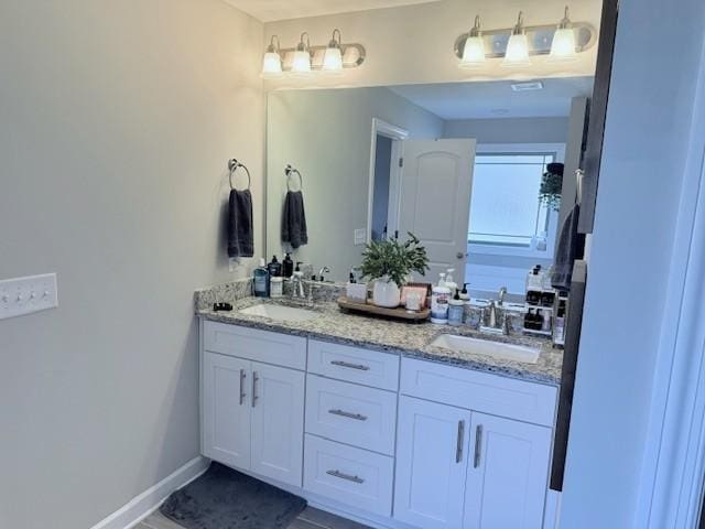 full bath with double vanity, baseboards, and a sink