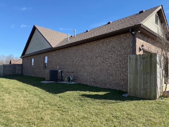 view of side of home with central AC unit, brick siding, fence, and a yard