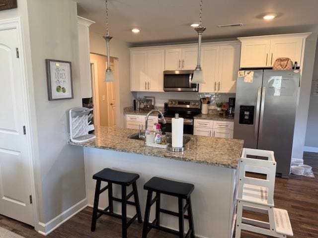 kitchen with appliances with stainless steel finishes, pendant lighting, white cabinets, and light stone countertops