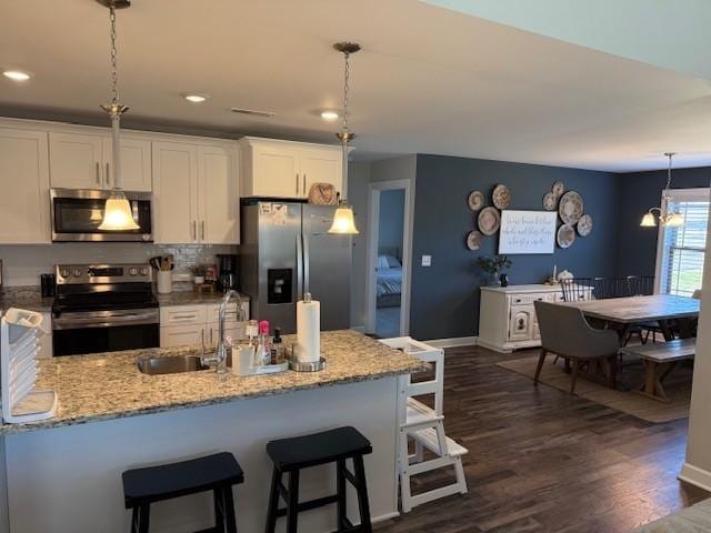 kitchen featuring dark wood finished floors, light stone countertops, stainless steel appliances, white cabinetry, and a sink