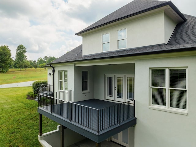 back of property featuring stucco siding, a lawn, and roof with shingles