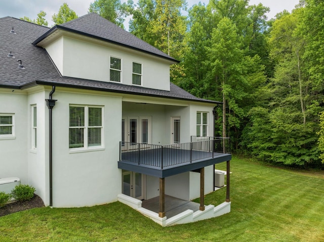 back of property with a shingled roof, central AC, a lawn, and stucco siding