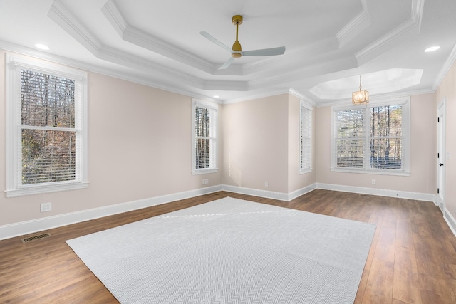 empty room featuring dark wood-style floors, a tray ceiling, ornamental molding, and baseboards