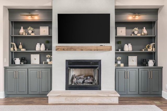 living room with dark wood-style floors, built in shelves, and a fireplace with raised hearth